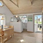 Dining room with wooden table, chairs, and windows. Kitchen and balcony are visible.