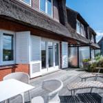 Terrasse mit Tisch, Stühlen und Liegestühlen vor einem Haus mit Schiebetüren und Dachreiter.