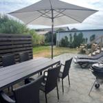 Terrasse mit Tisch, Stühlen, Sonnenschirm und Grill. Hintergrund: Garten und Zaun.