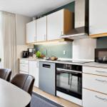 Küche mit weißen Schränken, Spüle, Herd und Mikrowelle. Tisch mit Stühlen und Fensterblick.