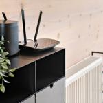 Router und Lautsprecher auf einem schwarzen Schrank vor einer Holzwand.