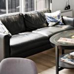 Schwarzes Ledersofa mit Kissen und Glas-Tisch mit Zeitschriften.
