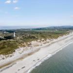 Aerial view of a coastal landscape with a lighthouse, dunes, and beach.