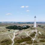 Weißer Leuchtturm auf Hügel mit Blick auf Küstenlandschaft und Himmel.