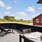 Terrasse mit Lounger, Tisch und Stühlen. Roter Holzausbau im Hintergrund.