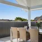 Terrasse mit Esstisch und Stühlen, dunkle Holzwände, Blick auf die Landschaft.