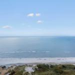 Ausblick auf Strand, Dünen und Leuchtturm an der Küste.