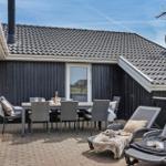 Terrasse mit Esstisch, Grill und Sicht auf grüne Bäume.
