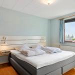 Ein Schlafzimmer mit Doppelbett, Fenster mit Vorhängen und Stuhl.