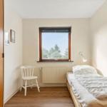 Flur mit Holzschrank, Tür zu Schlafzimmer mit Fenster und Blick auf Bäume.