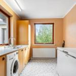 Bad mit Dusche, Waschbecken und Holzschränken. Fliesenwand und Fenster mit Pflanzen.