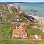 Haus mit Garten und Blick auf Strand. Mehrere Gebäude auf grünem Grundstück.