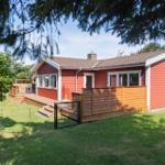 Rotes Holzhaus mit Terrasse und Garten. Holzgeländer und Schiebetüren sind sichtbar.
