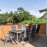 Terrasse mit Grill, Tisch und sechs Stühlen. Hintergrund: Holzzaun und grüne Bäume.