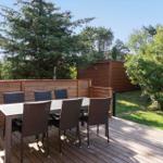 Terrasse mit Tisch und sechs Stühlen, umgeben von Grün und Holzgeländer.