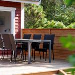 Terrasse mit Tisch und Stühlen vor einem roten Haus mit Holzgeländer.
