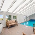 Innenpool mit Whirlpool und Sitzgelegenheiten unter Glasdach mit Blick auf Landschaft.