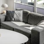Ein grauer Sofa mit Kissen und Decke vor einem Fenster mit Jalousien.