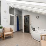 Dusche und Whirlpool unter einer Glasdachkonstruktion mit Sitzgelegenheiten und Pflanzen.
