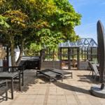 Glasveranda mit Sitzbereich und Tisch. Tür offen zur Terrasse. Grün hinter Glas.