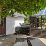 Terrasse mit Tischen, Stühlen und Sonnenschirm. Im Hintergrund Glasbau und Baum.