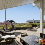Terrasse mit Liegestühlen, Tisch und Blick auf Grünfläche und Häuser.