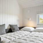 Schlafzimmer mit weißer Holzwand, Bett mit Kissen und Fensterblick auf Gras.