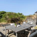Terrasse mit Tisch, Bänken und Weinflasche vor Gras- und Steinmauer.