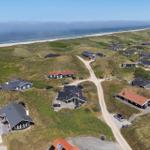 Dorf mit Häusern auf Dünen, Strand und Meer im Hintergrund.