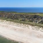 Aerielansicht einer Küstenlandschaft mit Strand, Dünen und Wohnhäusern.