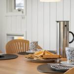 Esstisch mit Tassen, Kaffeebereiter und Gebäck auf dunklen Untersetzer.