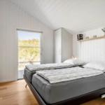 Schlafzimmer mit Doppelbett, weißer Wandverkleidung und Fenster zur Außenterrasse.
