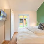 Schlafzimmer mit Bett, Fernseher und Blick auf Garten.