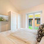 Schlafzimmer mit Bett, TV und Fenster zur Außenterrasse.