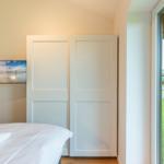 Schlafzimmer mit Bett, TV und Glasfront zum Garten.