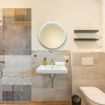 Badezimmer mit Dusche, Waschbecken und WC. Wand mit Mosaikfliesen und runder Spiegel.