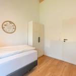 Schlafzimmer mit Bett, Kleiderschrank und Tür. Wanddekoration mit Pflanzenmotiv.