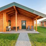 Holzhaus mit Terrasse, Tisch, Stühlen und Liegestühlen. Grasfläche und gepflasterter Weg.