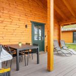 Terrasse mit Tisch, Stühlen und Liegen vor einem Holzhaus mit grüner Tür.