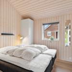 Bedroom with wooden wall cladding, bed with white pillows, and window view.