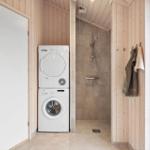 Washing machine and dryer in laundry room next to shower with wooden wall cladding.