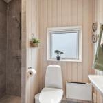 Bathroom with shower, toilet, and sink. Wooden wall, window, and towels.