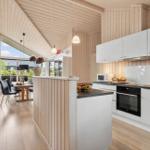 Kitchen with white cabinets, stainless steel fridge and oven. Wooden cladding and large window.