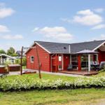 Red vacation home with terrace, garden, and hot tub under blue sky.