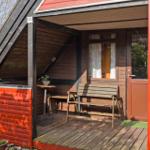 Roter Holzausbau mit Terrasse, Bank und Tisch. Tür und Fenster sind sichtbar.