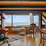 Wohnraum mit Holzdecke und Blick auf Wasser. Möbel und Einrichtung sichtbar.