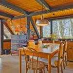 Esszimmer mit Holztisch, Stühlen und Blick auf Bäume. Holzwände und Deckenbalken.