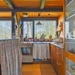 Küche mit Holzdecke, Fenstern und Küchenzeile mit Geschirr und Kochutensilien.
