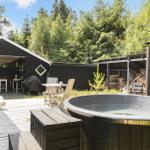 Backyard with hot tub, deck, and grill area. Surrounded by trees and woodpile.