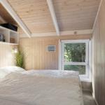 Bedroom with wooden walls and ceiling beams, bed with white bedding, window with view of forest.